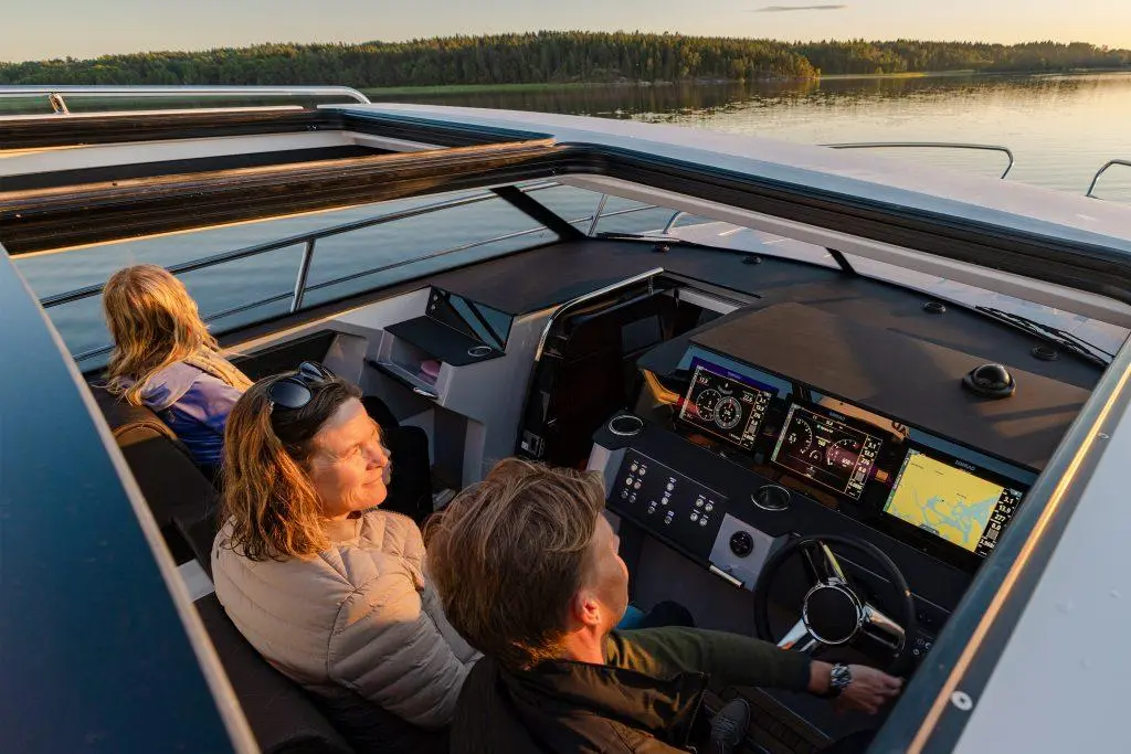 A group enjoying a boat ride, with a man steering at the helm featuring multiple navigation screens and sunset reflections.